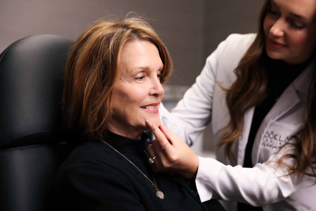 A Look Lab provider uses a mirror to show a female client what her facial skin will look like after having the best Hydrafacial in Denver.