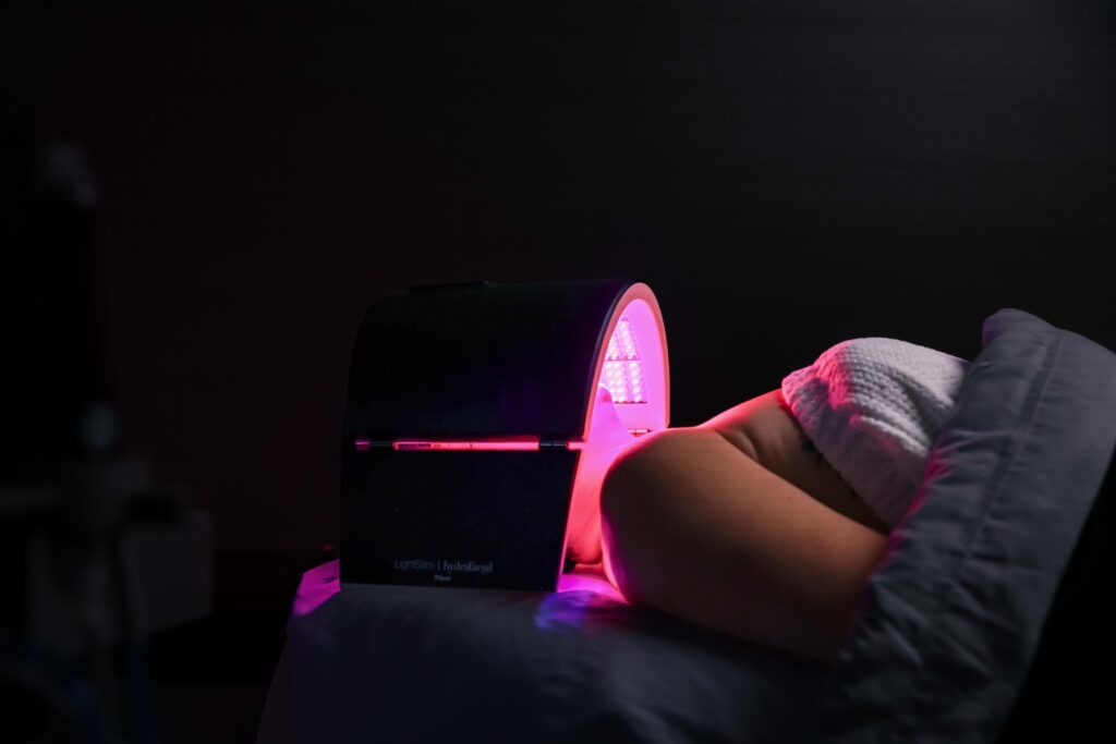 A patient lies on a comfortable treatment table as her face undergoes red light therapy. It supports the results of the best Hydrafacial in Denver.