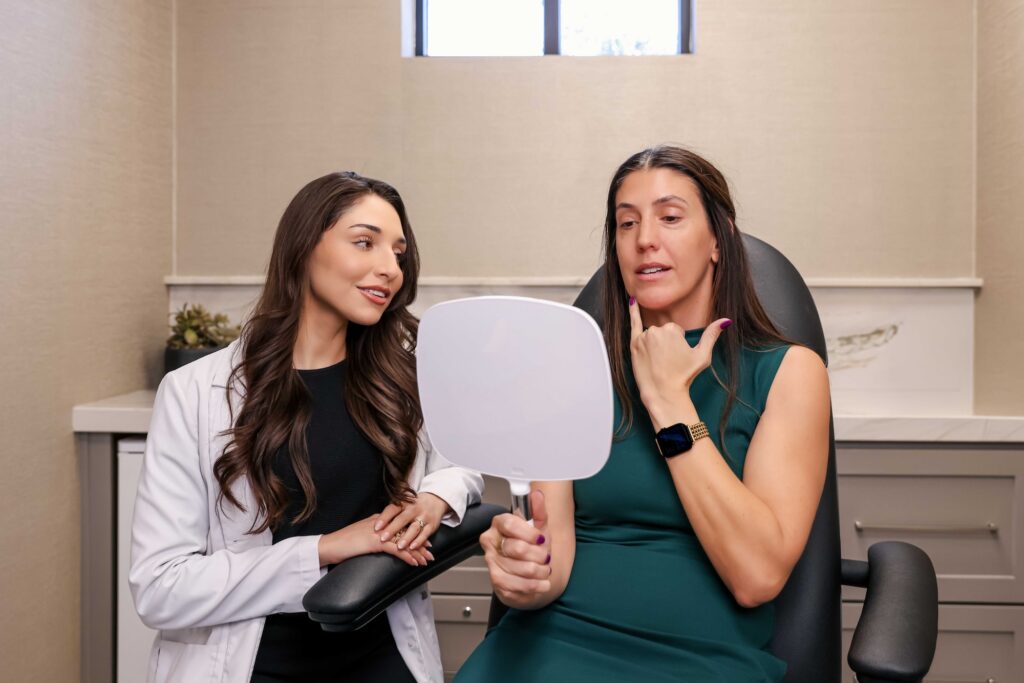 A female patient holds a mirror and points to her chin as a Look Lab provider explains her options for natural skin treatments in Winter Park.
